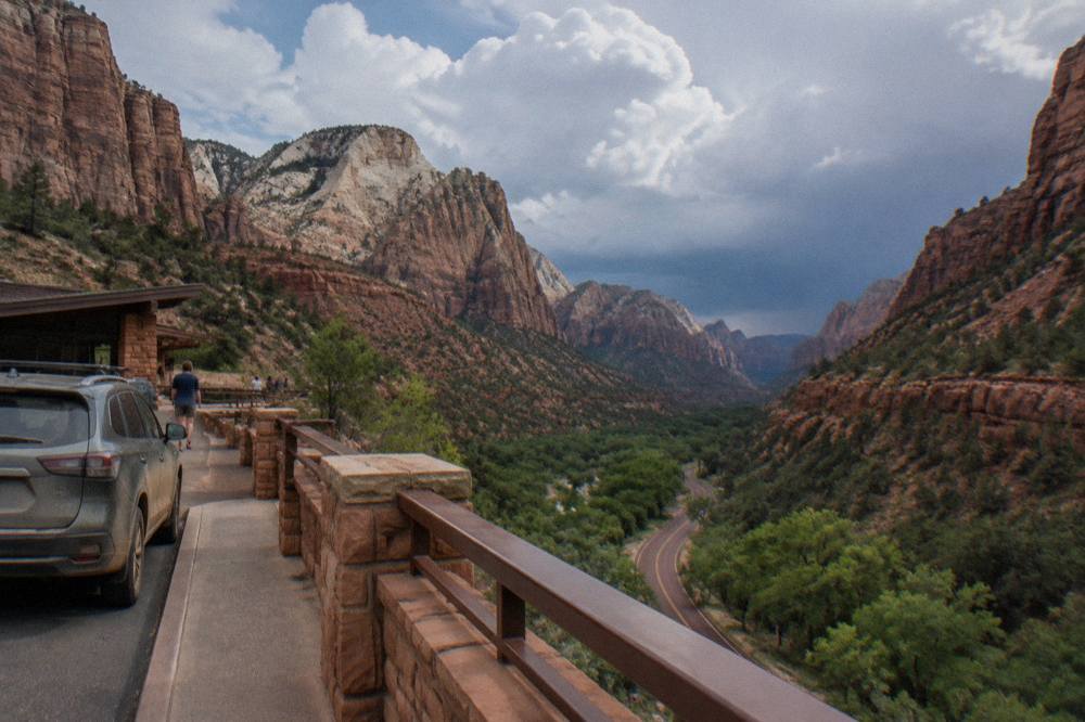 Layered sandstone cliffs above a green valley with a winding road