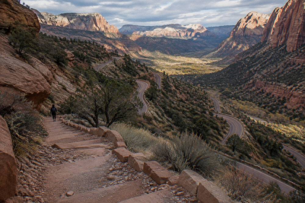 A winding road descending red rock switchbacks toward a wide desert valley with mesas on the horizon