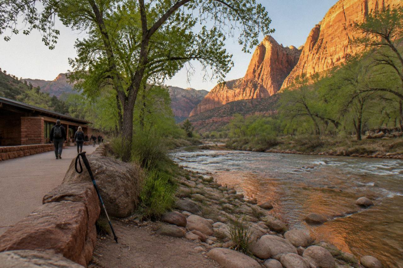 Red sandstone cliffs rising above a tree-lined river valley in southern Utah at golden hour