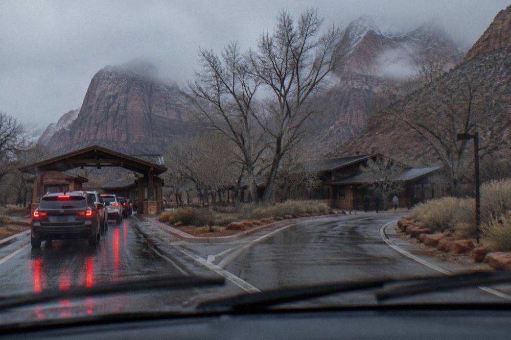 A line of cars waiting at a park entrance station beneath tall sandstone cliffs