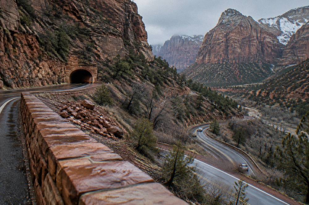 A paved road switchbacking down red sandstone slopes toward a tunnel entrance