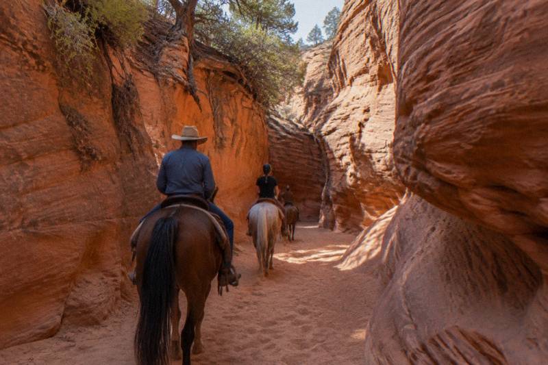 Horseback riders following a guide through a narrow red rock canyon in southern Utah