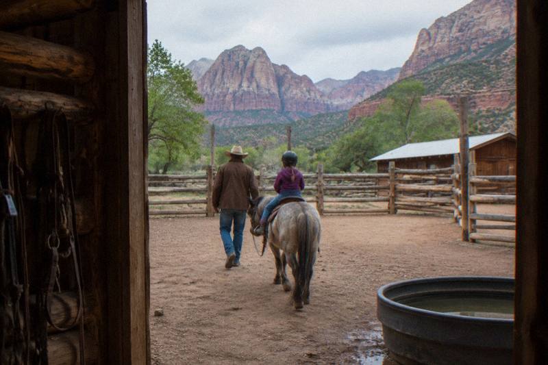 Family group horseback riding through a mountain meadow with red rock cliffs in southern Utah
