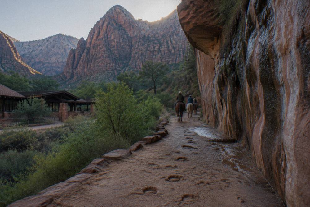 Red rock canyon walls above a sandy trail under a wide desert sky in morning light