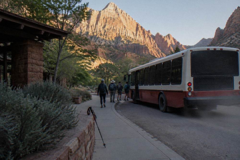 A shuttle bus at a canyon stop with red rock cliffs rising above the road