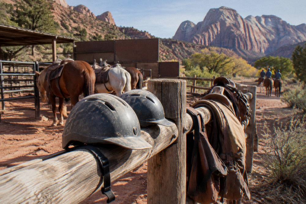 Riding helmets and saddle bags resting on a fence rail beside a red rock trailhead