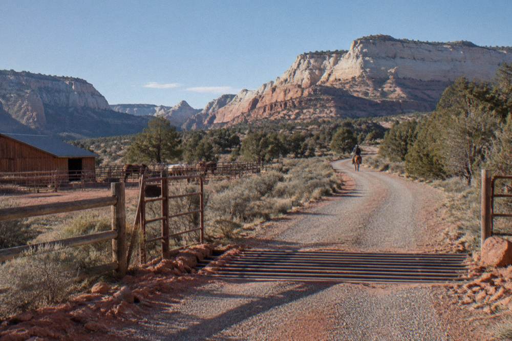 Gravel ranch road curving toward sandstone buttes under a wide desert sky