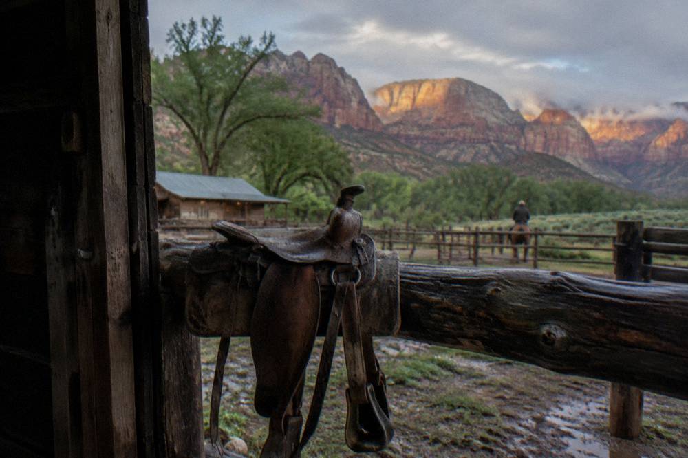 Empty western saddle resting on a rail fence with mesa cliffs behind