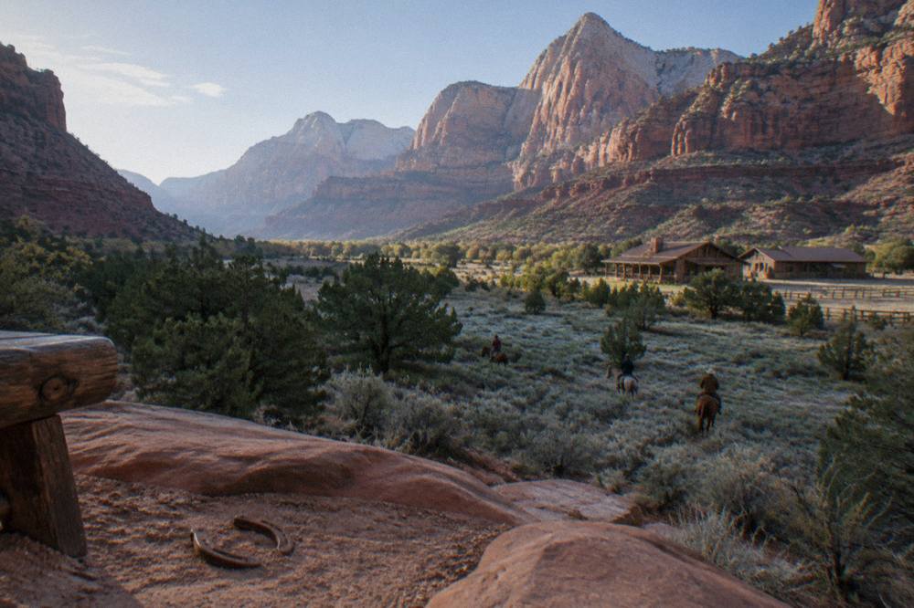 Sagebrush and juniper flats with layered red rock cliffs in the distance