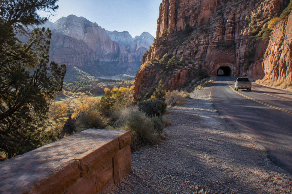 A two-lane desert highway curving toward tall sandstone cliffs