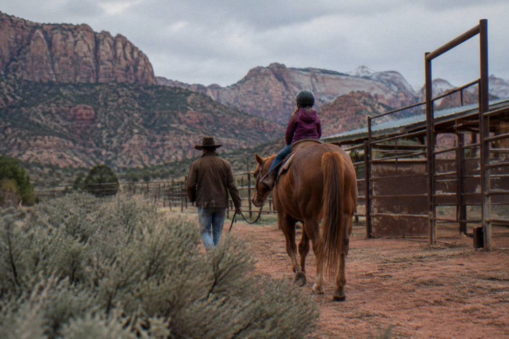 A child on a horse led by a wrangler along a dirt path