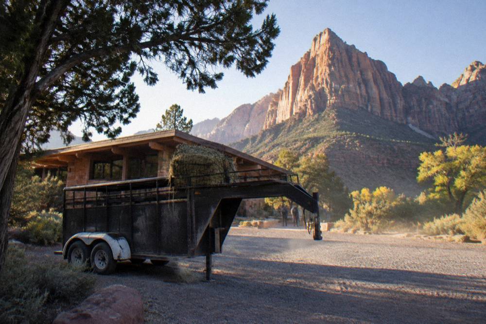 A horse trailer parked at a gravel trailhead with juniper scrub around it