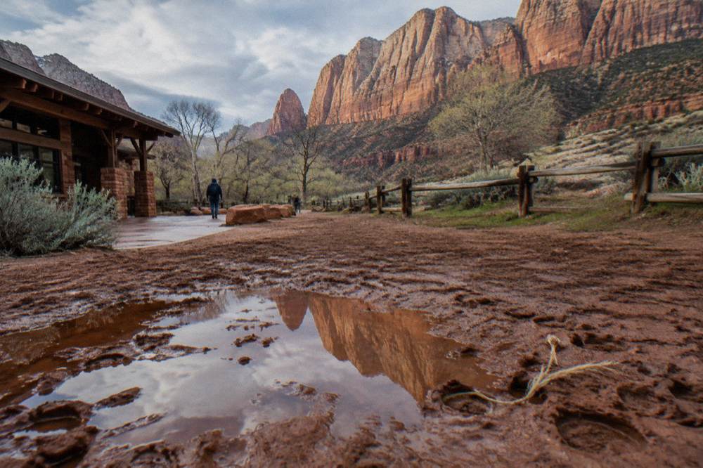 Wet red dirt trail with puddles reflecting a sandstone cliff face