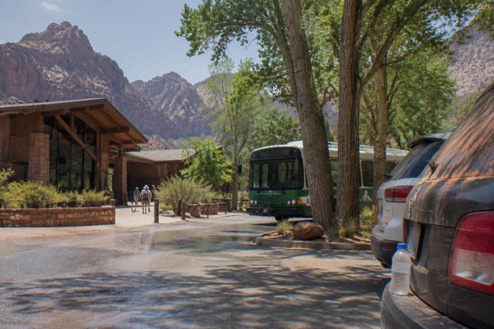 A parking area near a park lodge with a shuttle bus pulling up beside cottonwood trees