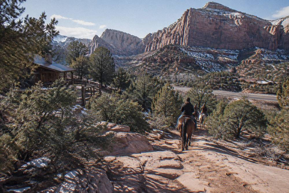 A horse trail winding through juniper and pinyon toward distant pink cliffs