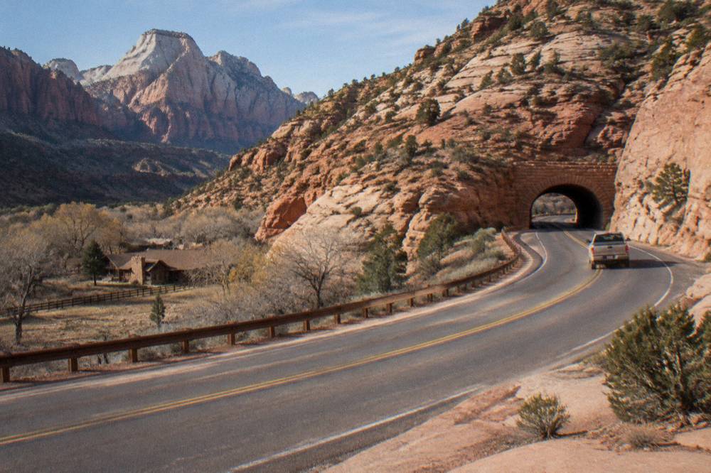 A paved mountain highway curving toward a sandstone tunnel entrance in dry desert country