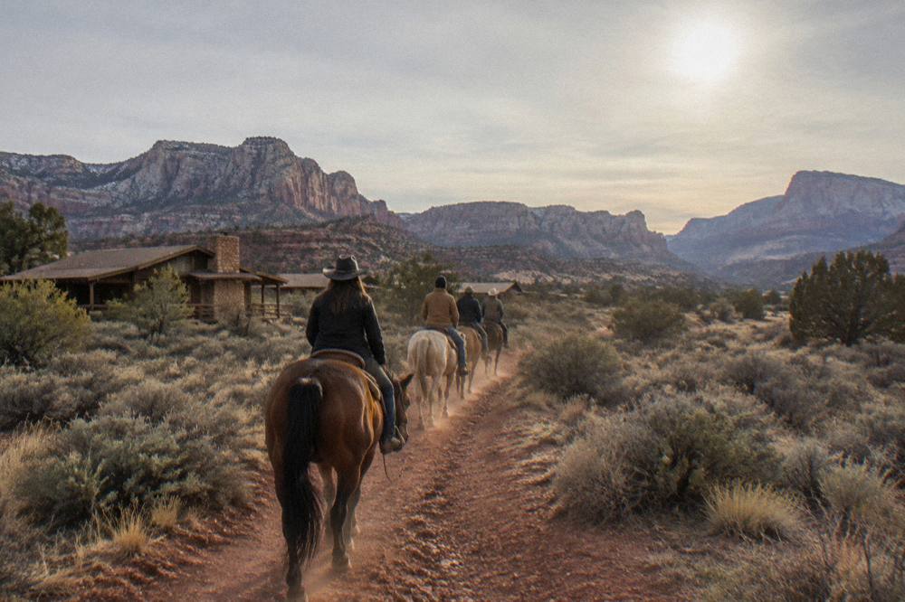 Riders on horseback crossing open high desert with distant layered plateaus